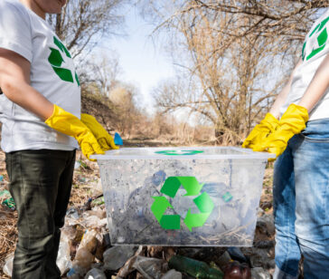 Boy and girl holding a container with garbage at plastic collection in a polluted clearing, recycling signs on the T-shirts